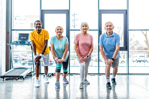 cheerful senior multiethnic sportspeople synchronous stretching at gym