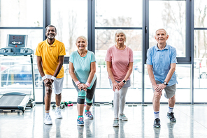 happy senior multiethnic sportspeople synchronous stretching at sports hall