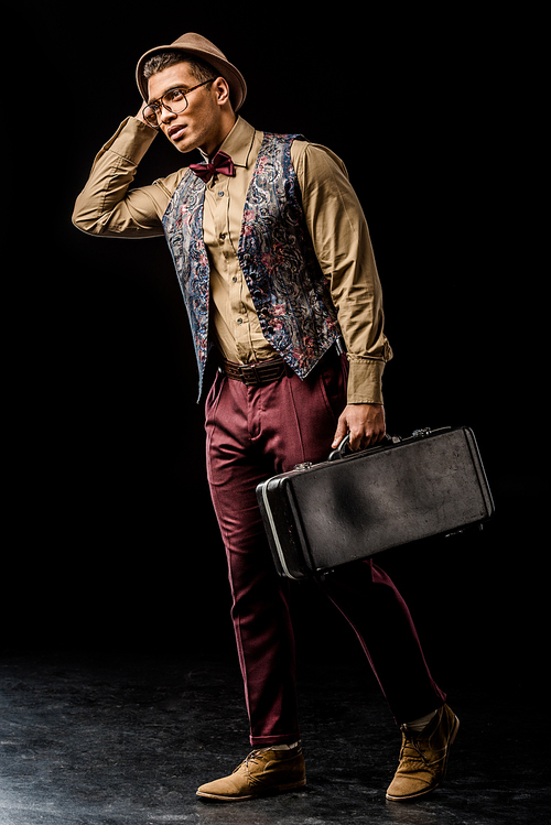 handsome mixed race young male jazzman posing with trumpet case on black