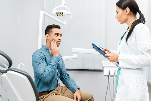 female dentist standing near  african american patient with toothache