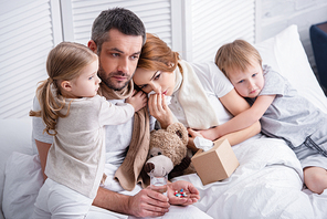 adorable siblings hugging sick parents in bedroom