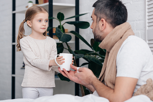 adorable daughter giving cup of tea to sick dad in bedroom