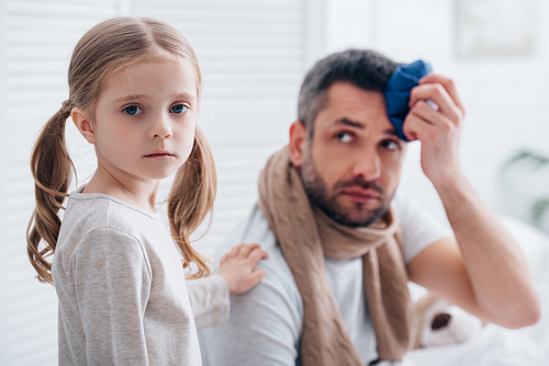 daughter supporting sick father touching head with ice pack in bedroom