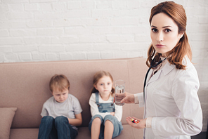 pediatrist holding pills and glass of water for sick children in living room