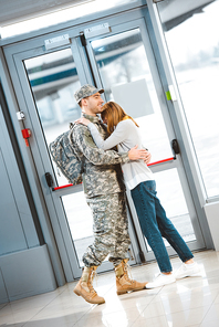 happy girlfriend hugging smiling boyfriend in military uniform in airport