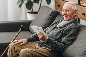 happy pensioner with grey hair looking at photos and sitting on sofa