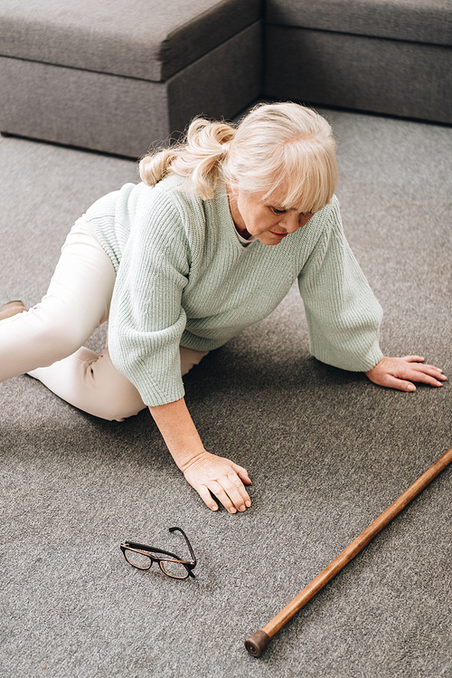 helpless senior woman with blonde hair sitting on floor at home