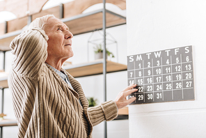 senior man touching wall calendar and head