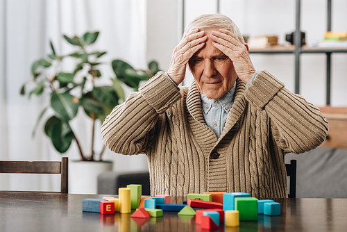 retired man having headache while sitting near wooden toys at home