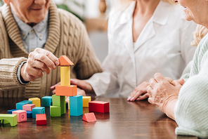 cropped view of caregiver sitting with retired man and woman and playing with wooden toys