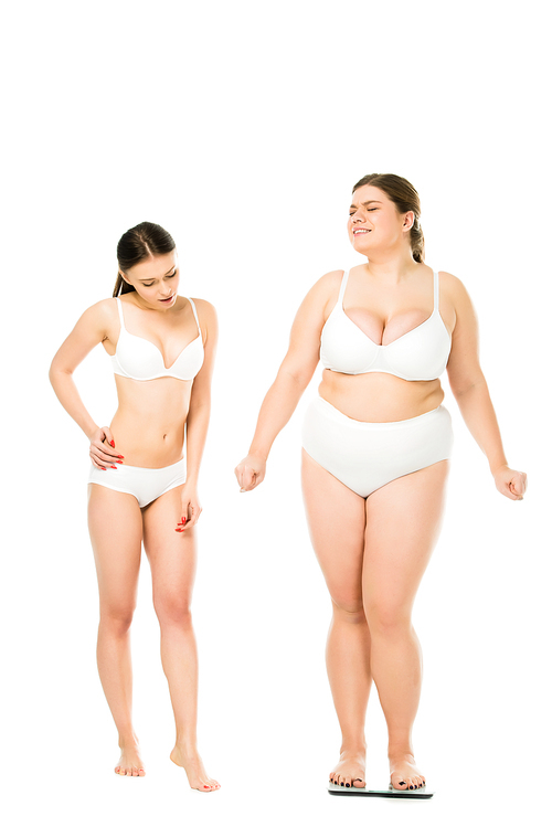 shocked slim woman in underwear looking at happy overweight woman on scales isolated on white, body positivity concept