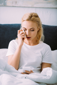 crying woman wiping tears and using smartphone in bed at home