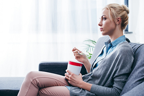 sad woman eating ice cream while siitng on couch at home alone with copy space