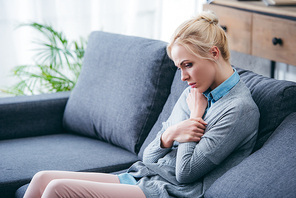 sad woman in casual clothes sitting on couch at home