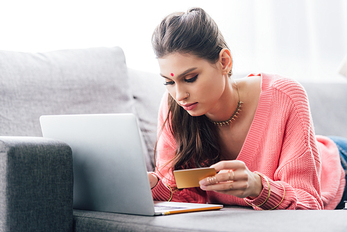 attractive indian woman with bindi shopping online with laptop and credit card