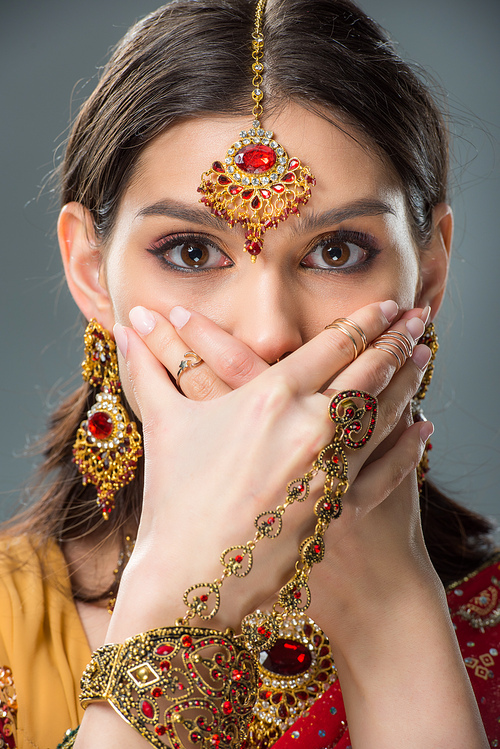 shocked indian girl closing mouth with hands, isolated on grey