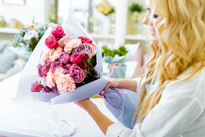 partial view of female florist holding bouquet with roses and carnations in flower shop