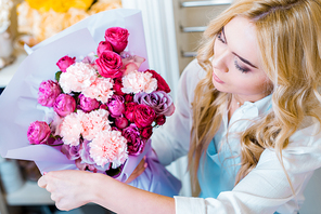 beautiful blonde woman holding flower bouquet with roses and carnations in flower shop