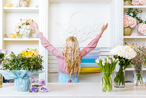 back view of female florist with hands in air in flower shop