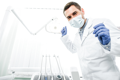 dentist in latex gloves and mask holding dental instrument and dental lamp