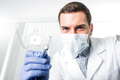 concentrated dentist in latex gloves and mask holding dental instrument in hand