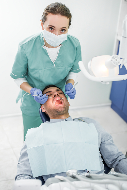 female dentist in mask and latex gloves working with patient with opened mouth