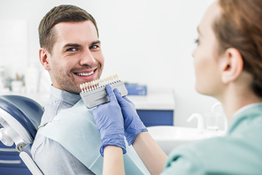 selective focus of happy man smiling near dentist with teeth color palette in hands