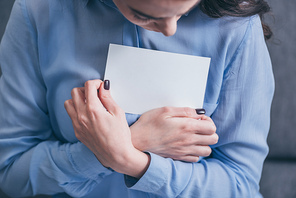 cropped view of woman in blue blouse holding and hugging photo in room, grieving disorder concept