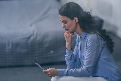 grieving woman propping chin and looking at photograph at home with copy space