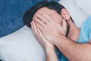 grieving man in bed covering face with hands and crying at home