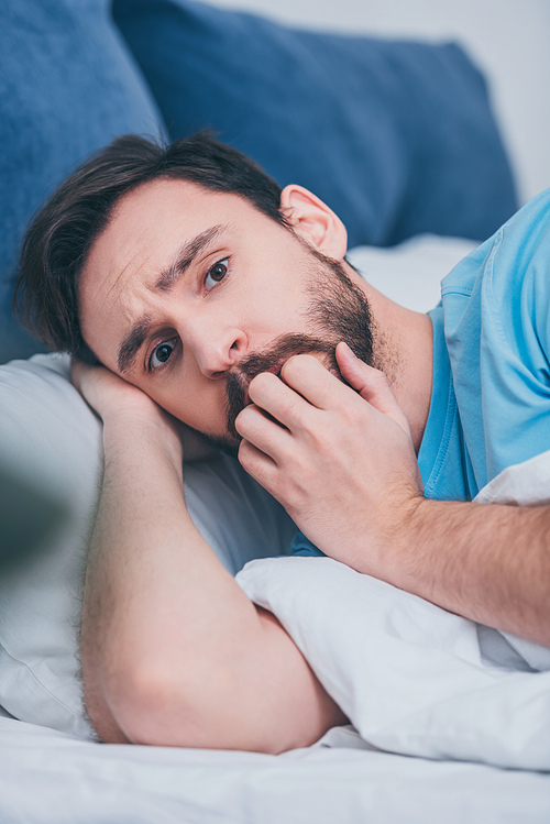 scared man lying in bed,  and covering mouth with hand