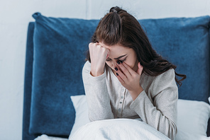 depressed woman crying and wiping tears while lying in bed at home