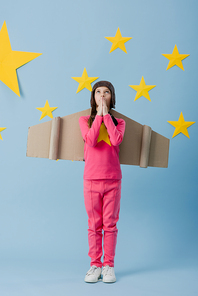 Full length view of kid with cardboard wings looking up on blue starry background