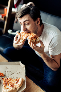 hungry man eating tasty pizza in living room