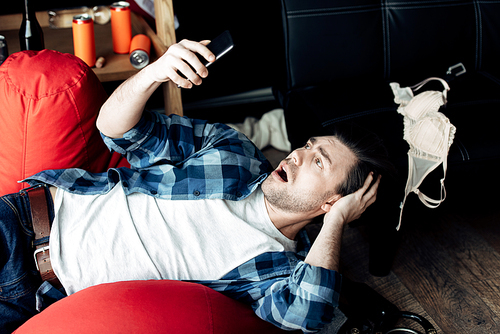 surprised man lying on bean bag and looking at smartphone