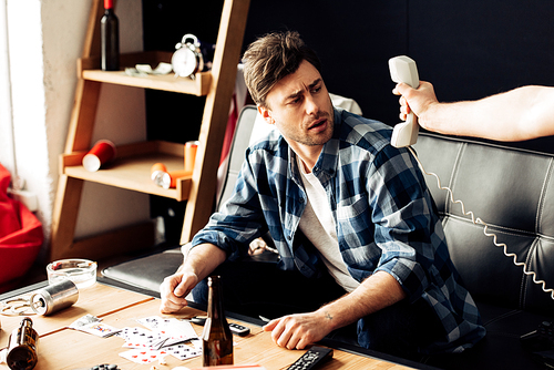 cropped view of man holding retro phone in hand near drunk friend sitting on sofa