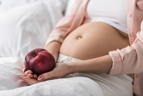 Cropped view of pregnant woman with red apple