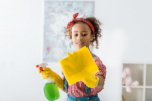 cute african american child holding yellow rag and green spray bottle