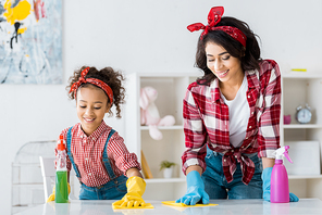 happy african american mom with adorable daughter cleaning table in bright rubber gloves