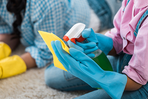 cropped view of african american child spraying cleaning liquid on yellow rubber rag