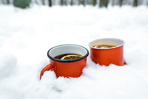 two cups of tea with lemons standing on white snow near trees in snowy forest