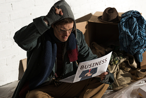 affected homeless man reading business newspaper while sitting surrounded by rubbish