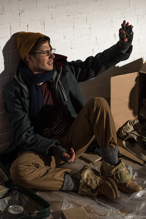 homeless beggar man sitting by brick wall and waving hand