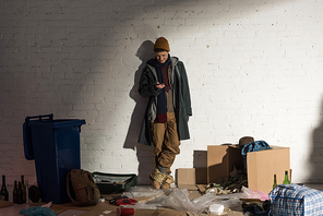 homeless man using smartphone while standing on rubbish dump