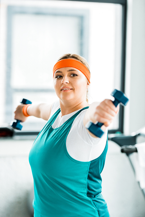 selective focus of cheerful overweight woman workouting in sportswear with dumbbells