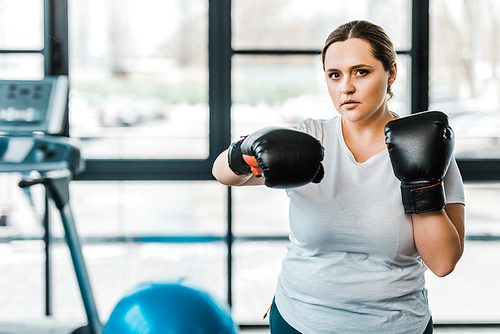 serious overweight woman wearing boxing gloves practicing kickboxing in gym