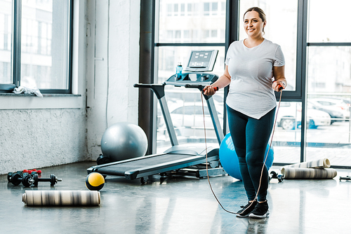 cheerful plus size woman standing with jumping rope in gym