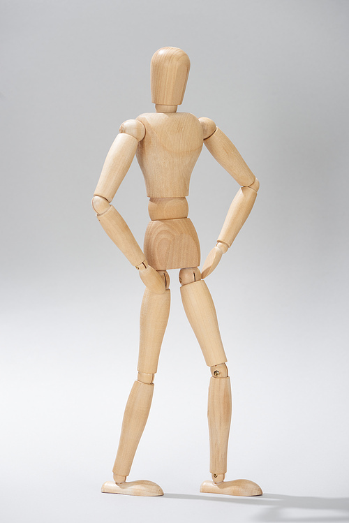 Wooden puppet with akimbo pose on grey background
