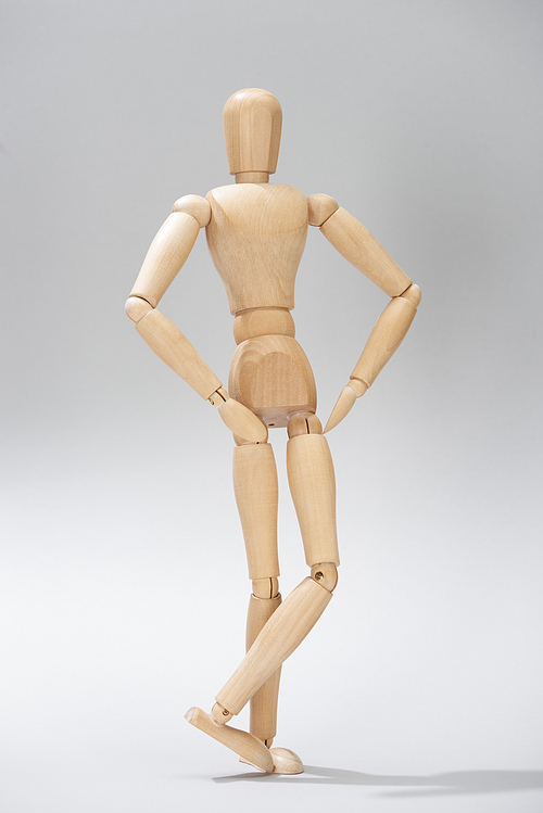 Wooden doll with hands on hips on grey background