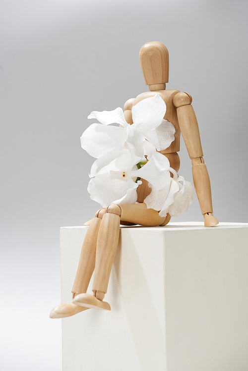 Wooden doll with orchid flowers on cube on grey background